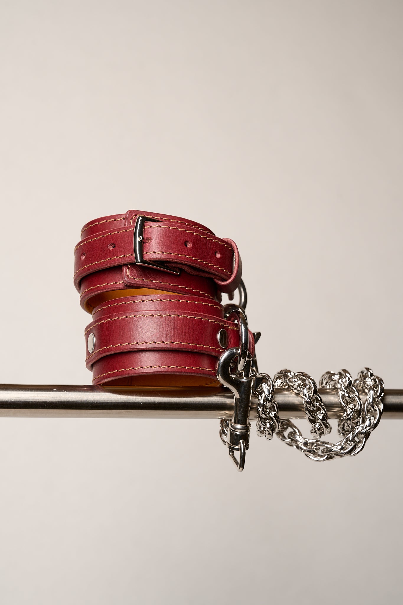 Red leather wrist cuffs with a chain on a white background