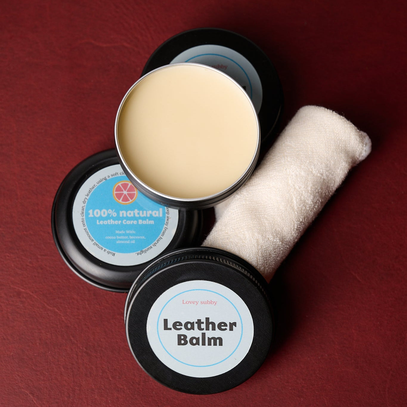 leather balm tin open with cotton cloth on burgundy background