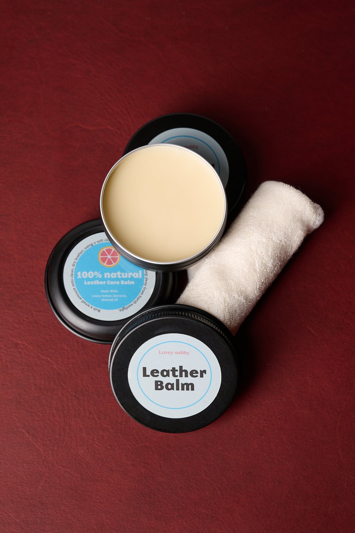 leather balm tin open with cotton cloth on burgundy background
