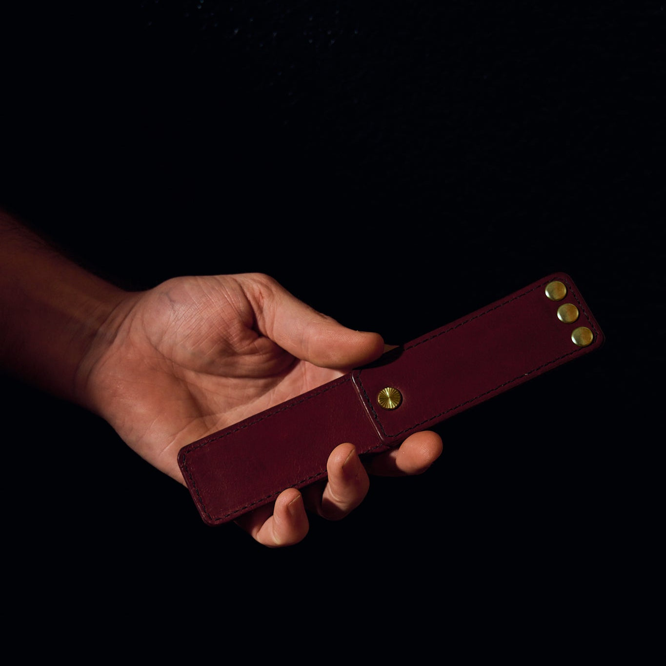 mans hand holding burgundy leather novelty item on black background
