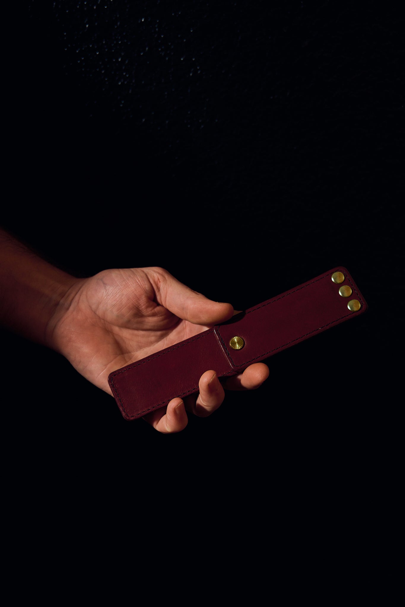 mans hand holding burgundy leather novelty item on black background