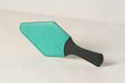 Turquoise paddle with black handle on a beige background