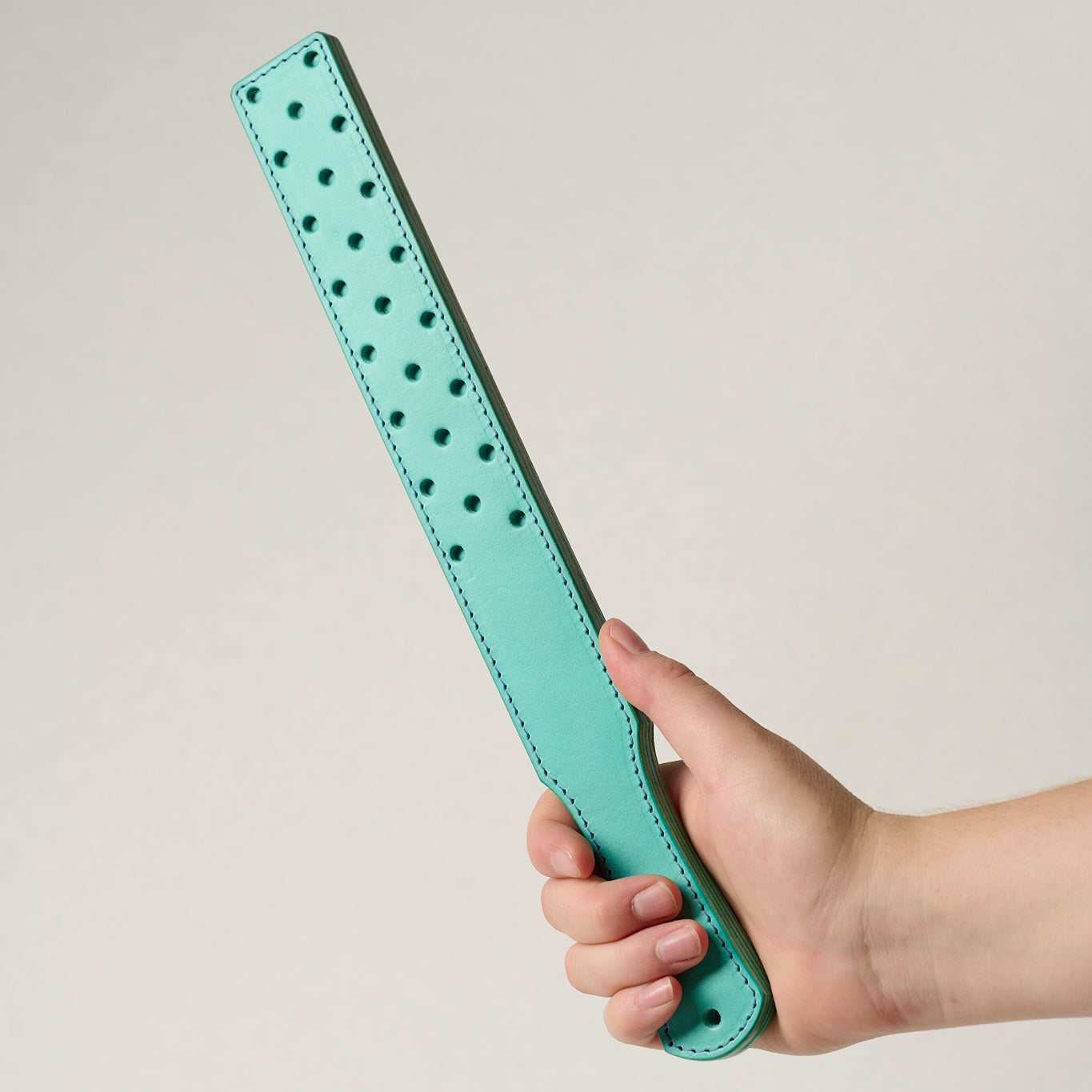 Turquoise leather belt with small holes held by a hand on a light gray background