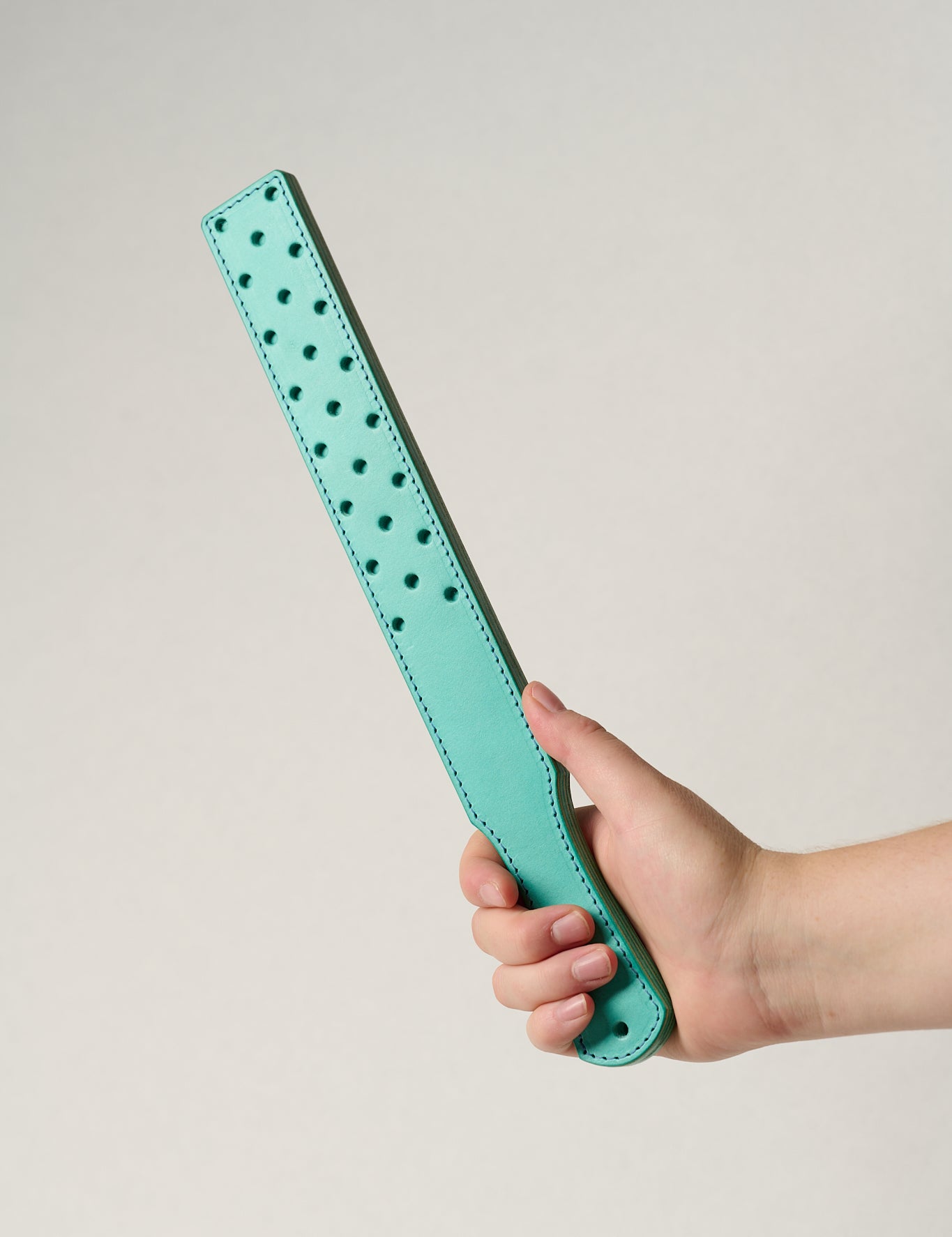 Turquoise leather belt with small holes held by a hand on a light gray background