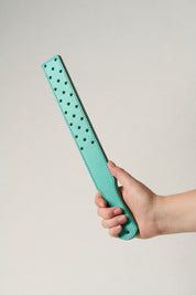 Turquoise leather belt with small holes held by a hand on a light gray background