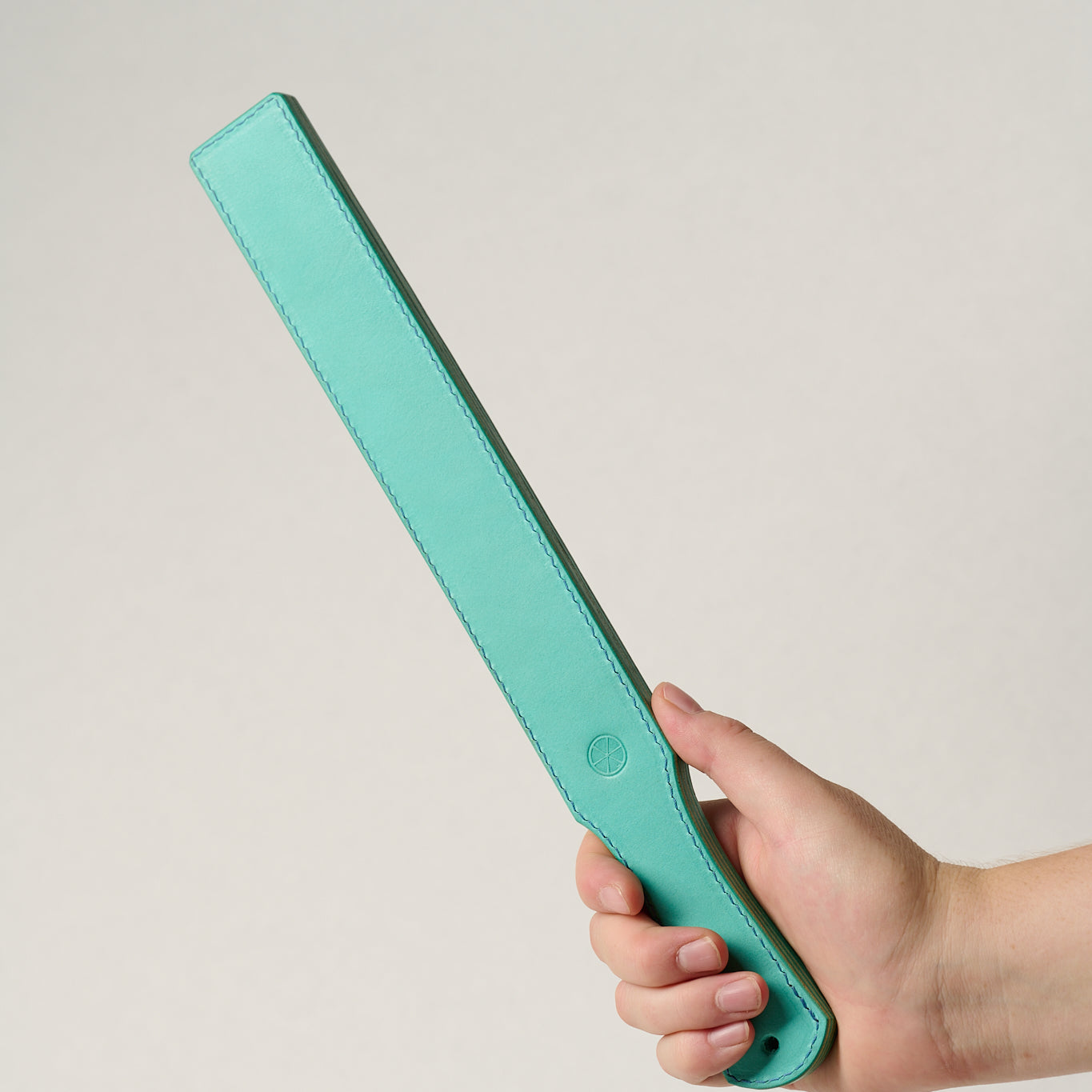 Hand holding a turquoise rectangular leather belt against a light gray background