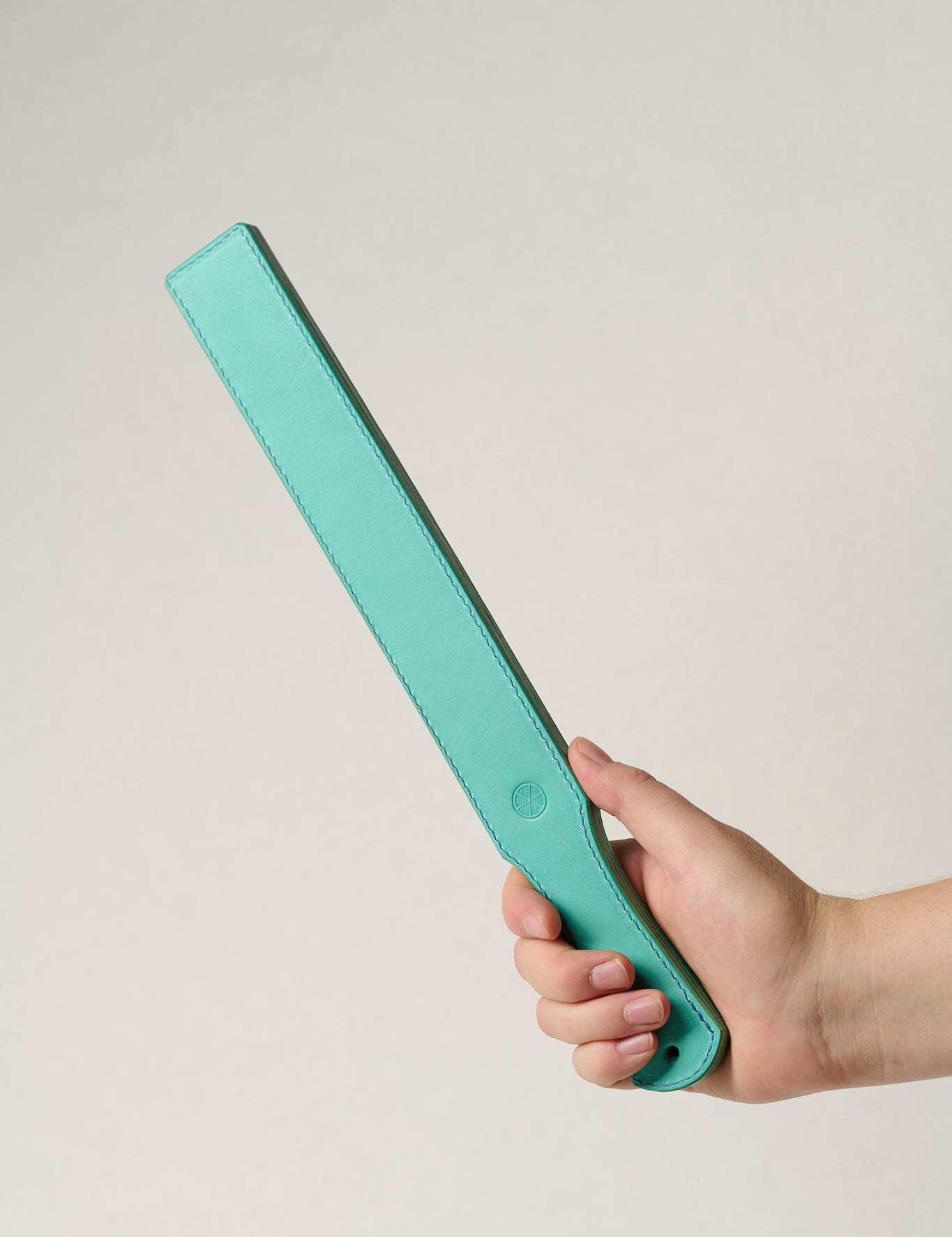 Hand holding a turquoise rectangular leather belt against a light gray background