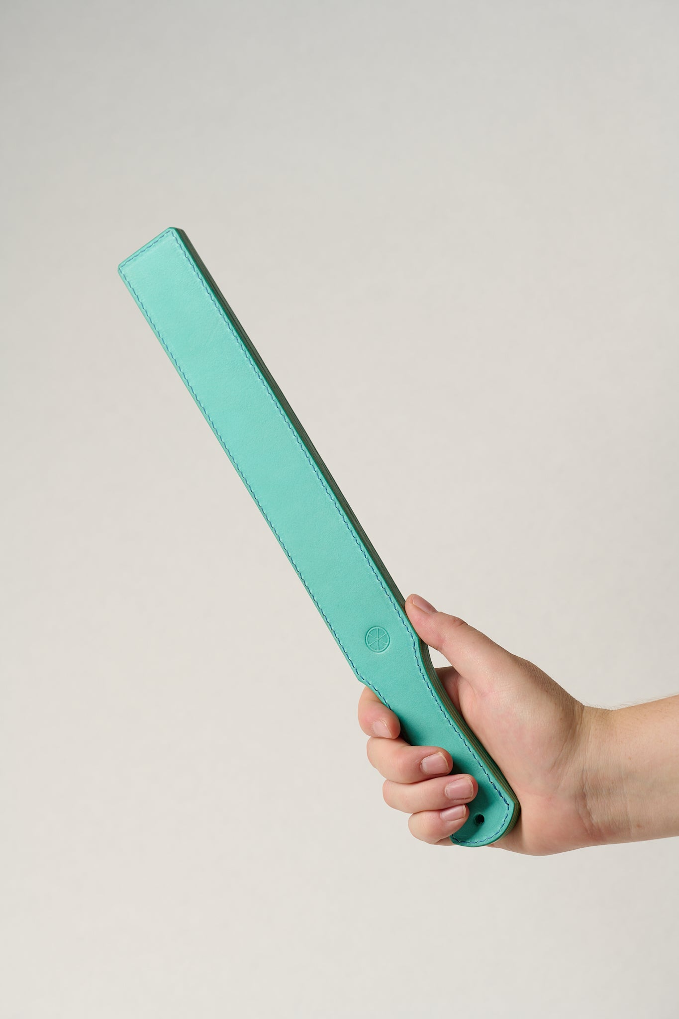 Hand holding a turquoise rectangular leather belt against a light gray background