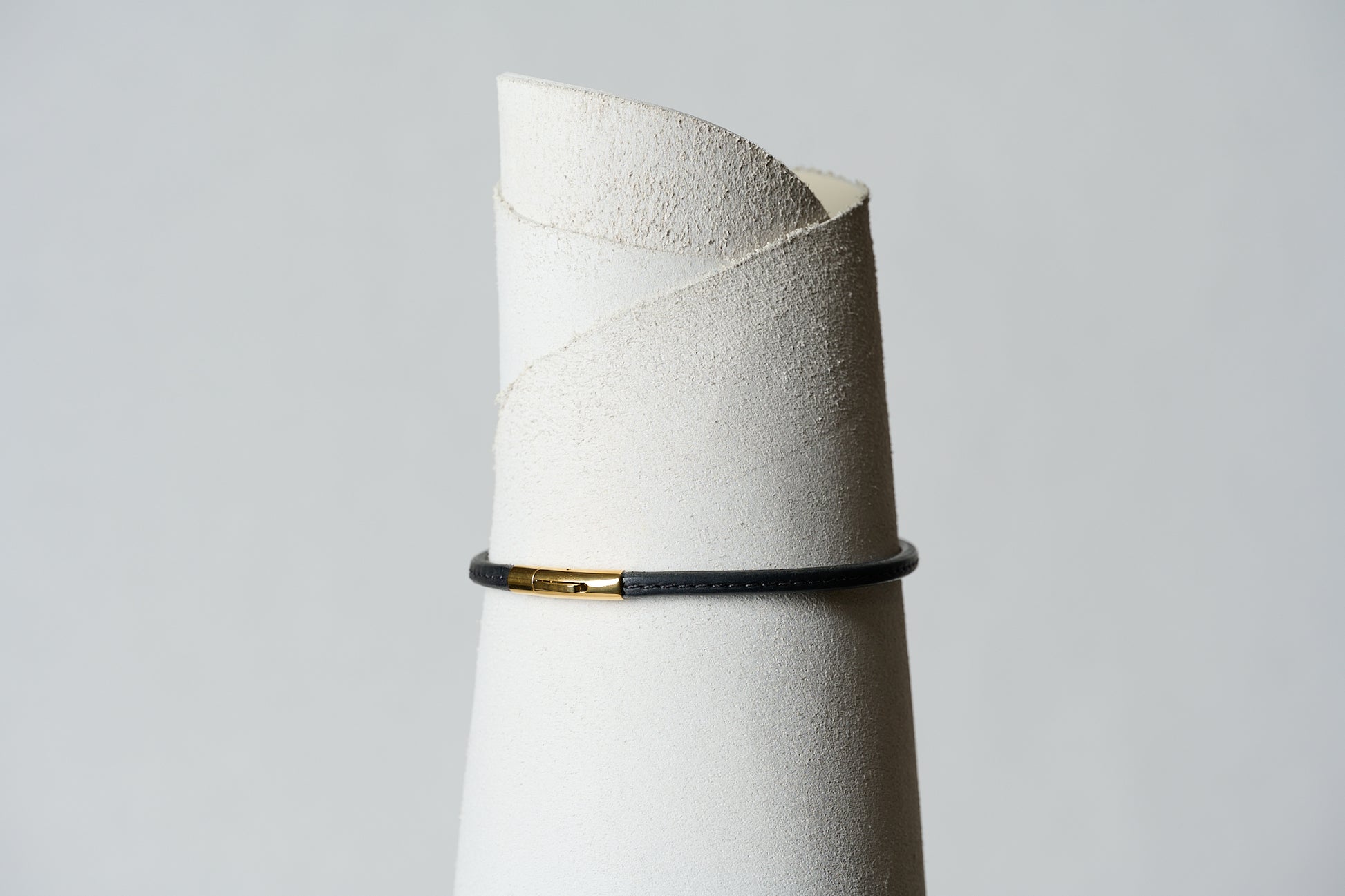 Black leather single continual ring closed with a gold clasp and stitched with black thread down the center.