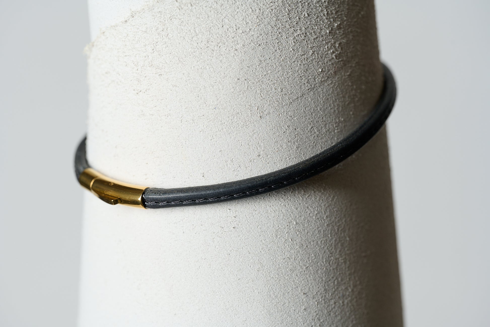 Black leather single continual ring closed with a gold clasp and stitched with black thread down the center.