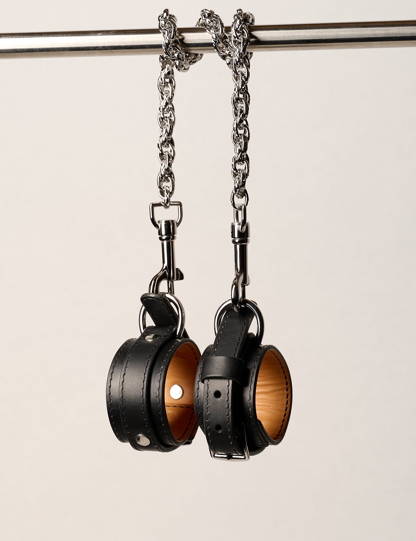 Pair of black leather wrist cuffs on a metal chain against a light background