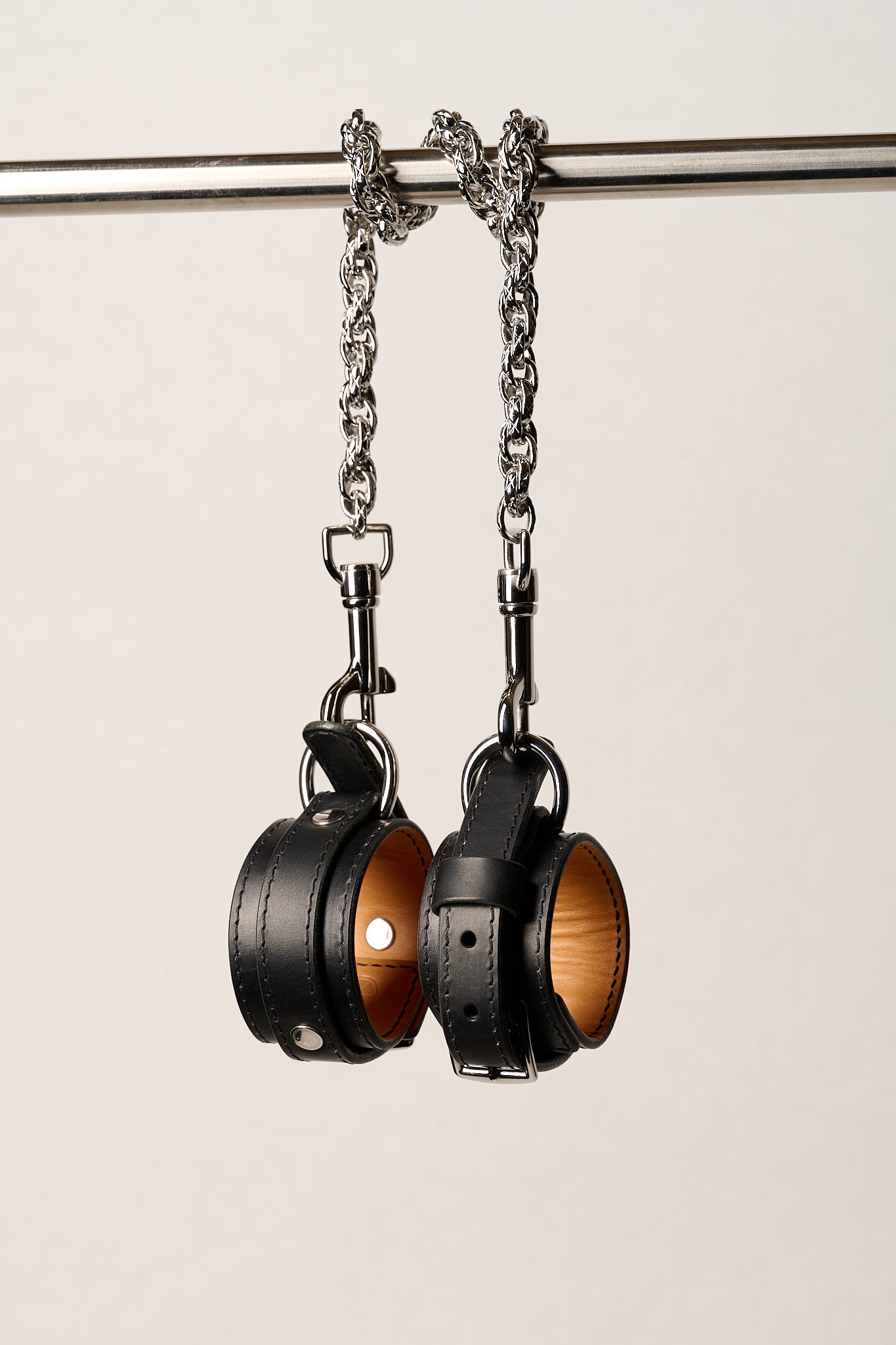 Pair of black leather wrist cuffs on a metal chain against a light background
