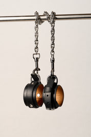 Pair of black leather wrist cuffs on a metal chain against a light background