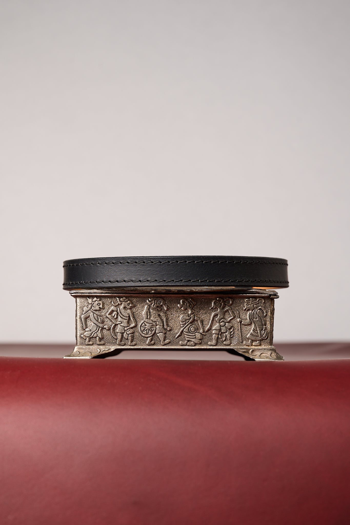 Black leather necklace on decorative metal box with embossed designs on a red surface