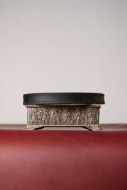 Black leather necklace on decorative metal box with embossed designs on a red surface