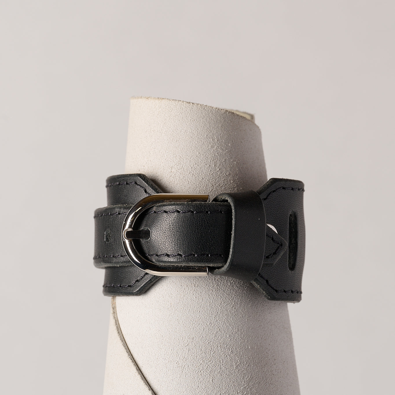 Black leather bracelet on a white roll of leather against a light gray background