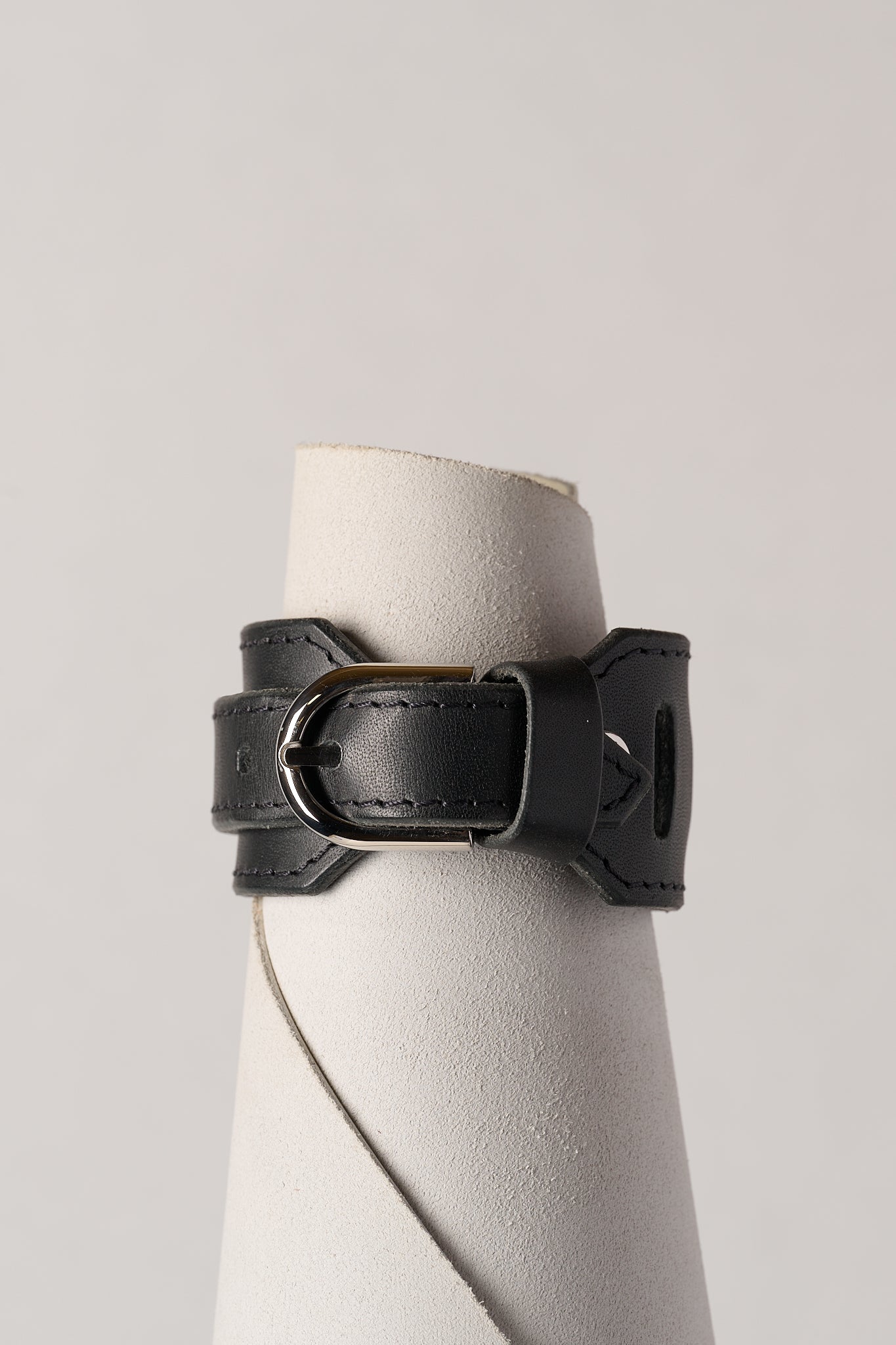 Black leather bracelet on a white roll of leather against a light gray background