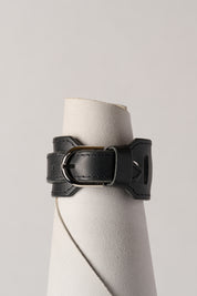 Black leather bracelet on a white roll of leather against a light gray background