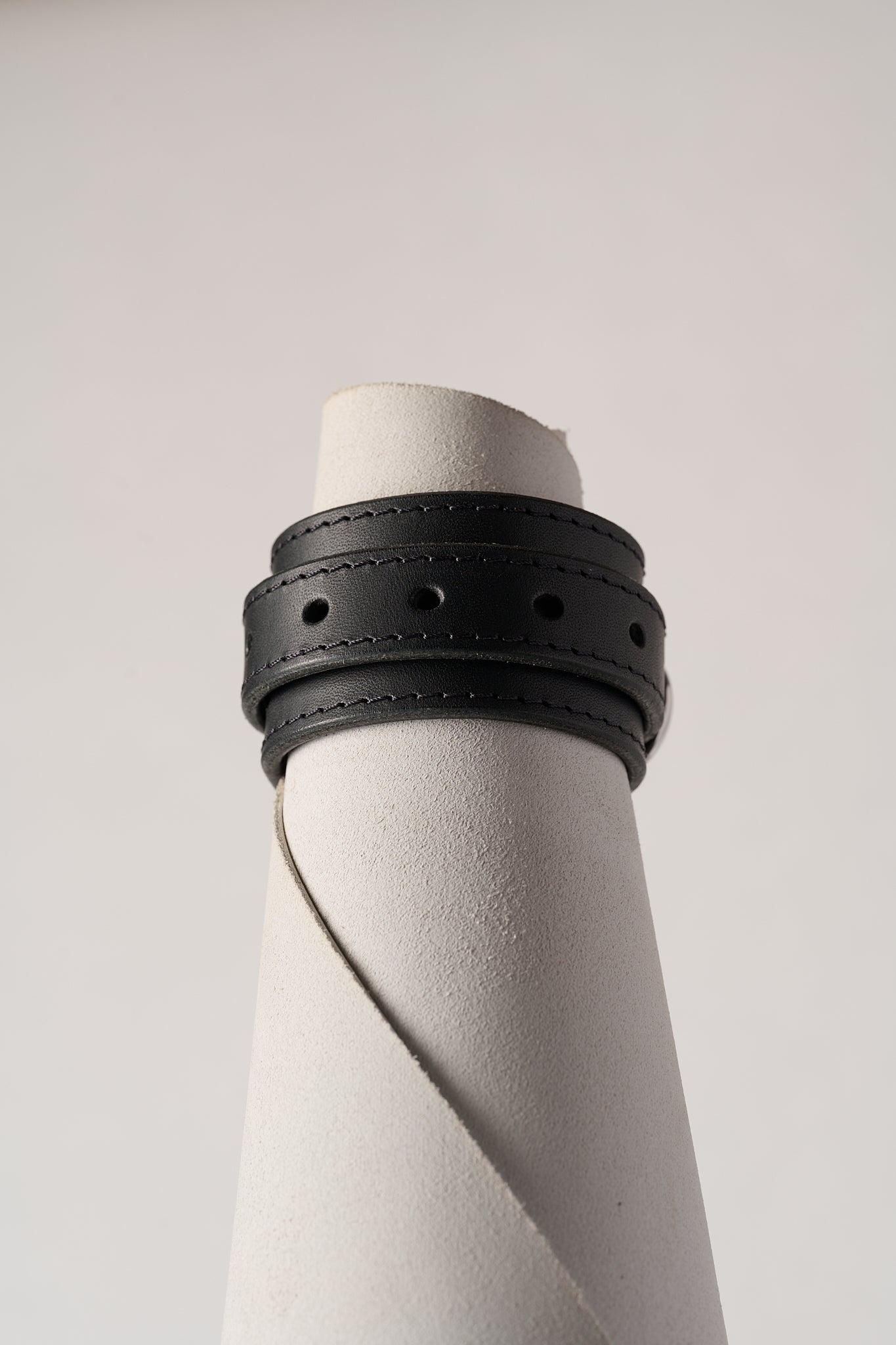 Black leather bracelet on a white cylindrical object against a light gray background