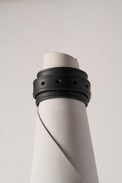Black leather bracelet on a white cylindrical object against a light gray background