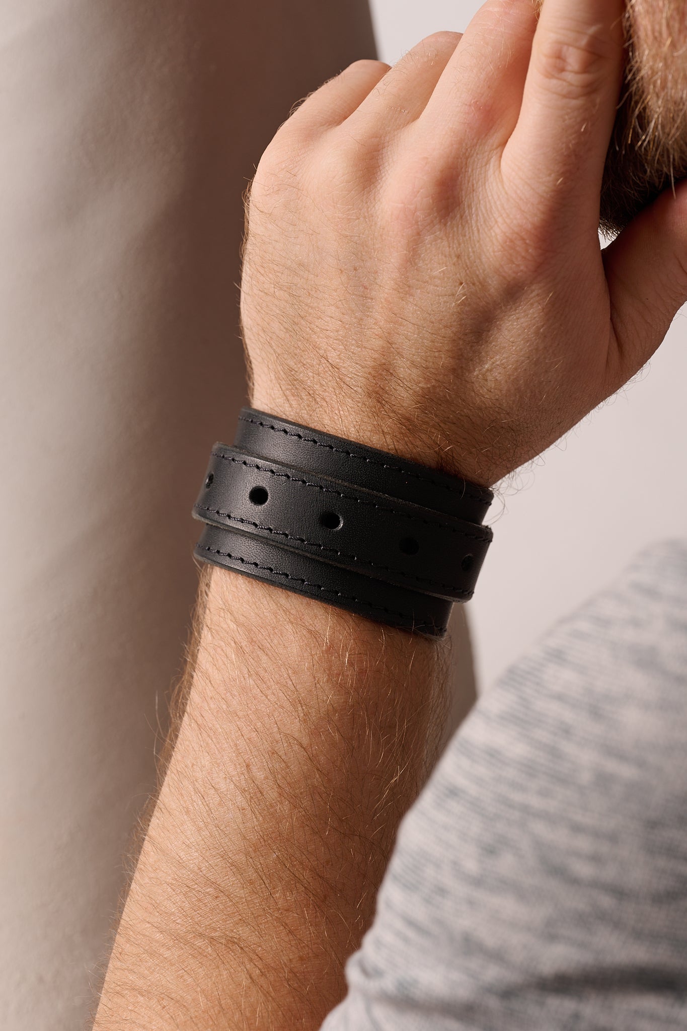 Close-up of a person's wrist wearing a black leather bracelet against a neutral background