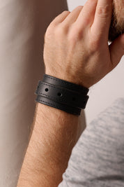 Close-up of a person's wrist wearing a black leather bracelet against a neutral background
