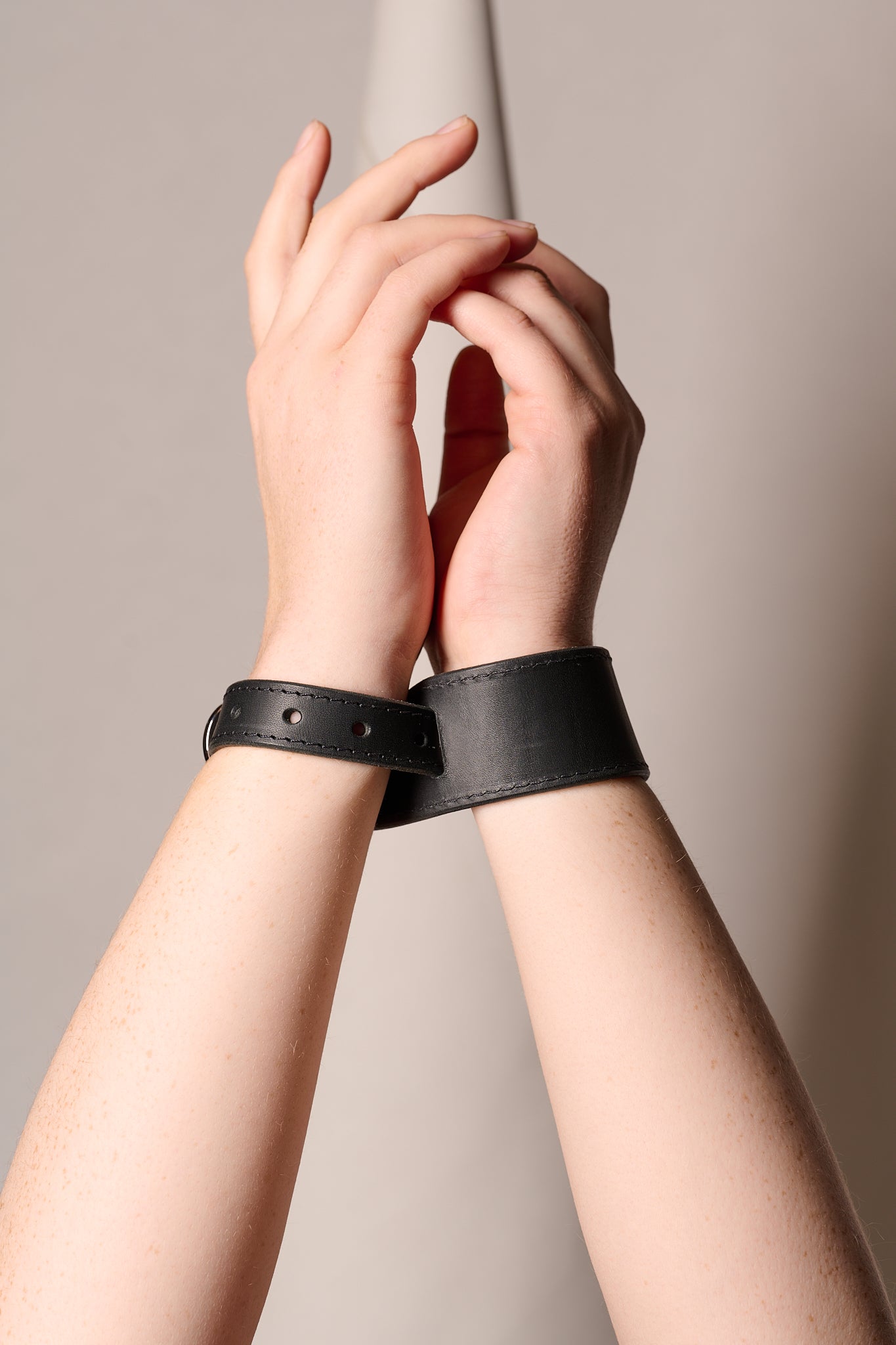 Two hands wearing black leather cuffs against a neutral background