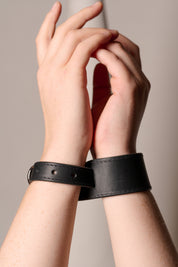 Two hands wearing black leather cuffs against a neutral background