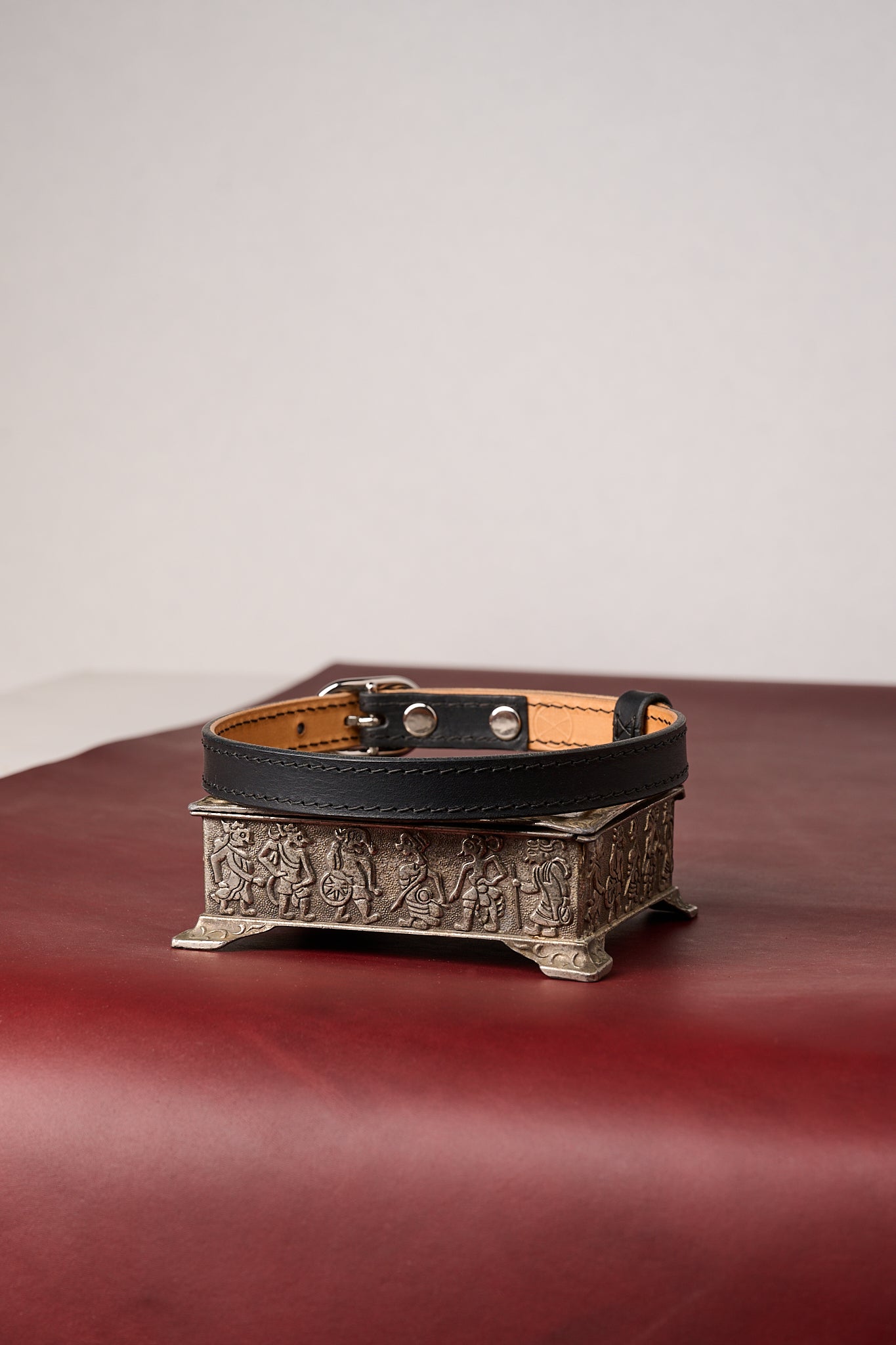 Black leather choker necklace on a decorative metal stand with a plain background