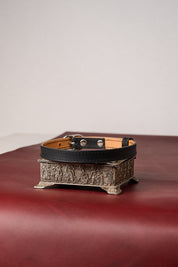 Black leather choker necklace on a decorative metal stand with a plain background