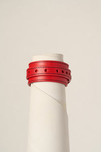 A red leather wrap bracelet displayed on a white cylindrical mannequin stand against a light beige background.
