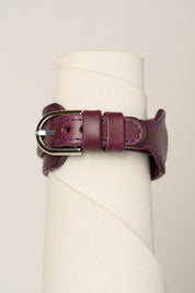 A dark purple leather watch strap with a silver-toned metal buckle, wrapped around a white cylindrical display stand.