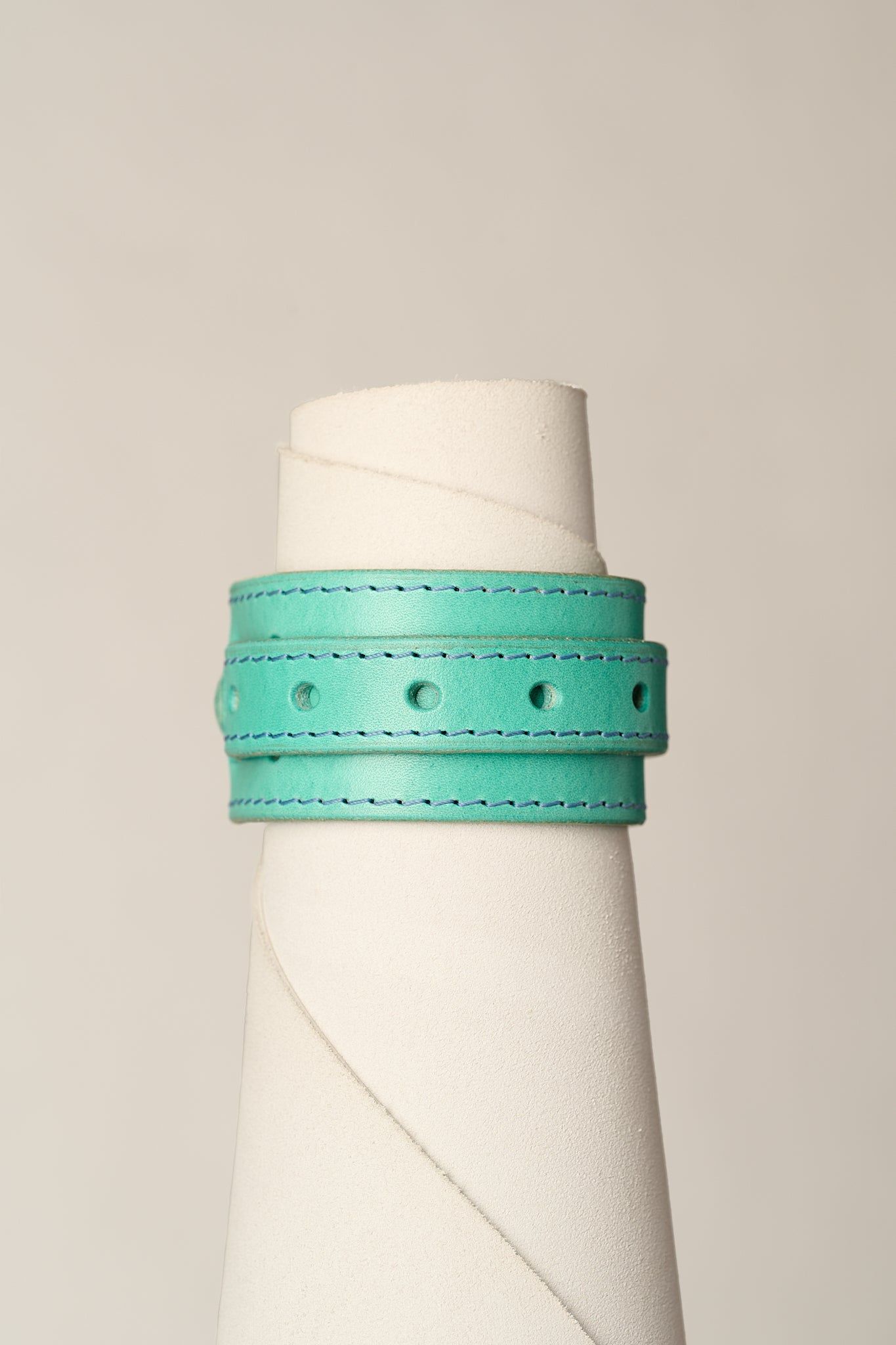 A turquoise leather wrap bracelet with matching stitching and metal eyelets, displayed on a white cone mannequin against a light gray background.