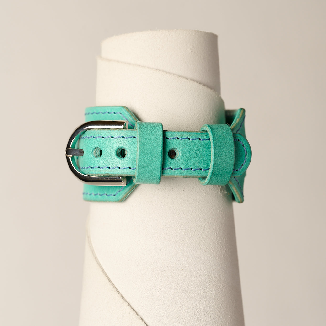 A mint green leather bracelet with a silver-toned metal buckle, displayed on a white cylindrical mannequin stand against a light beige background.