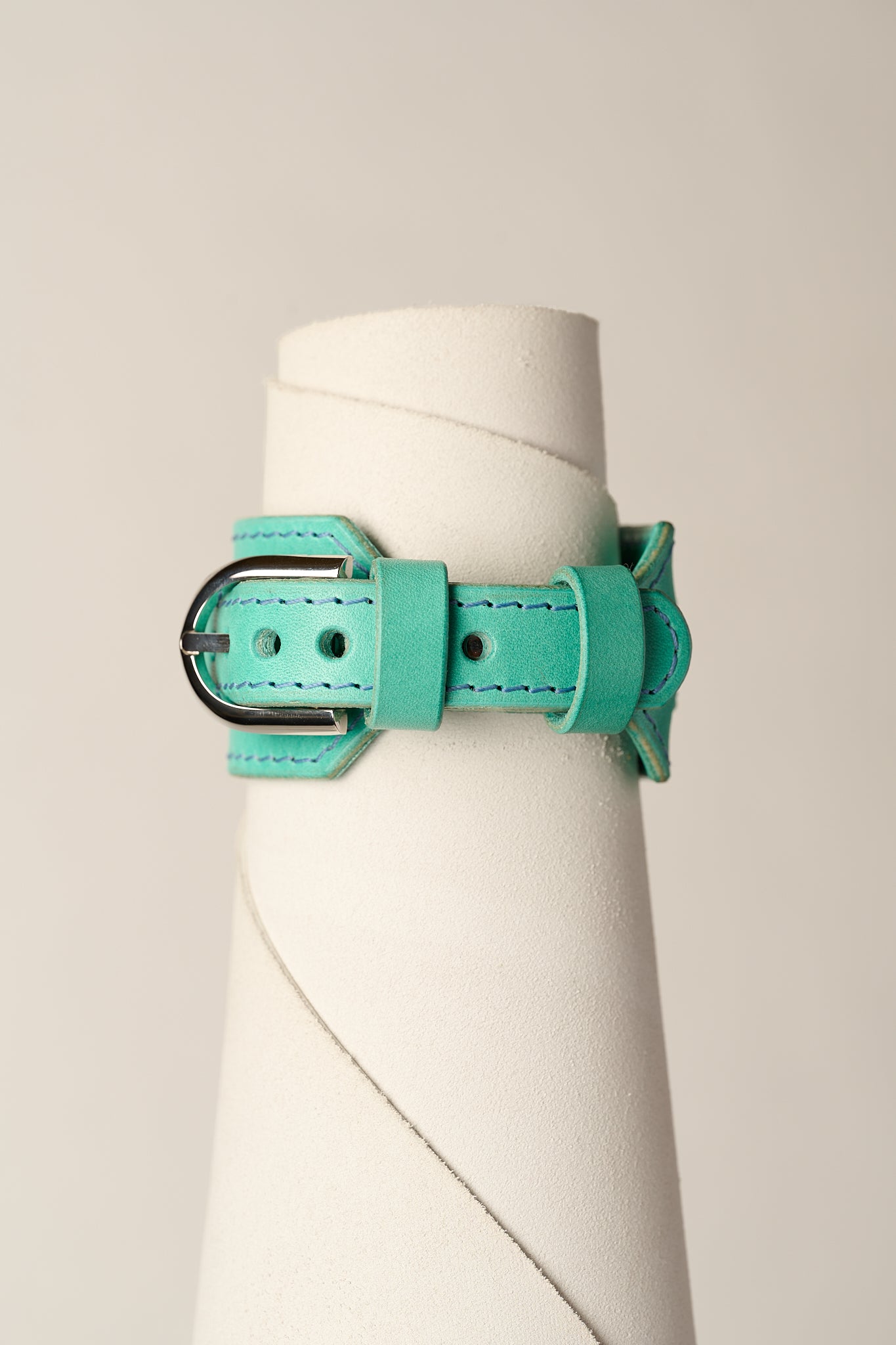A mint green leather bracelet with a silver-toned metal buckle, displayed on a white cylindrical mannequin stand against a light beige background.
