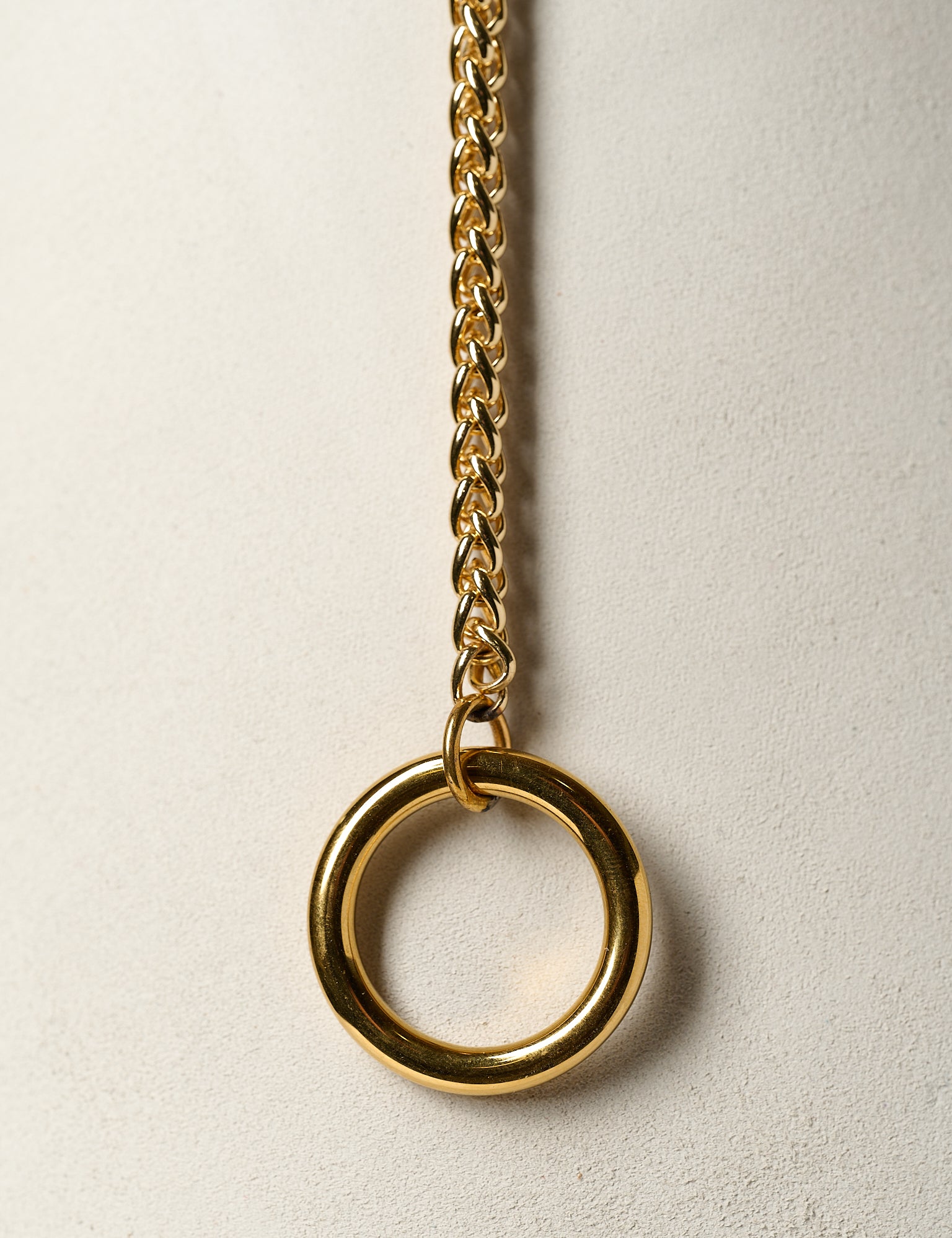 Gold chain necklace with a large ring pendant on a light beige background