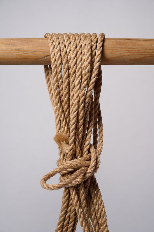 Natural Lovey Subby shibari Jute rope wrapped around and hanging from a wooden pole.