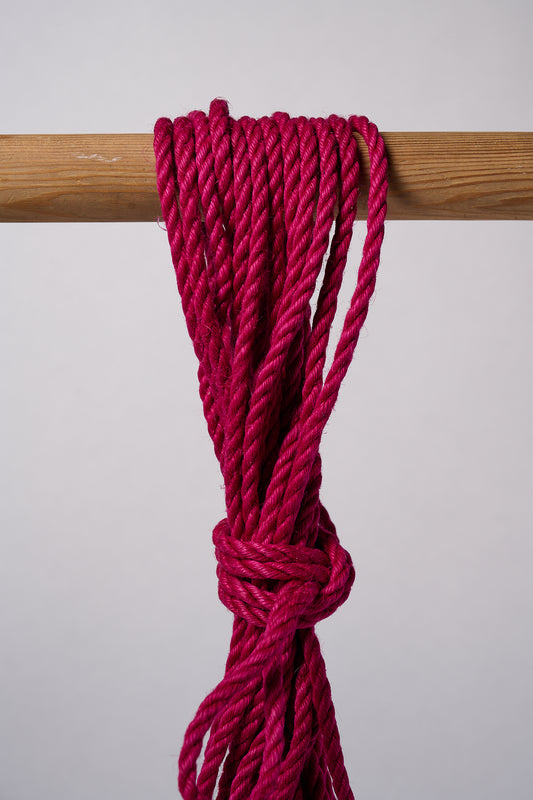 Pink Lovey Subby jute rope knotted and hanging over a wodden rod.