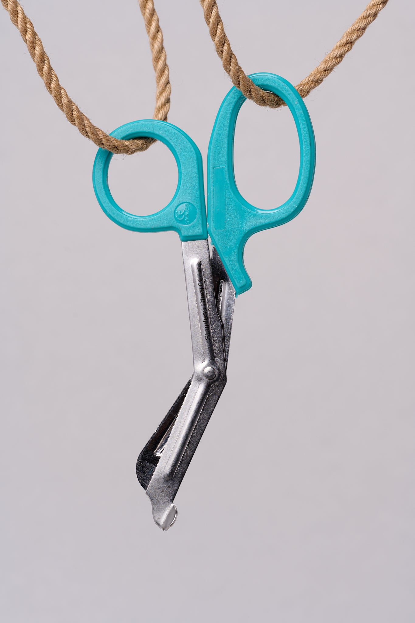 Silver emergency shears with light teal handles hanging from natural jute rope.
