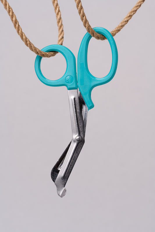Silver emergency shears with light teal handles hanging from natural jute rope.