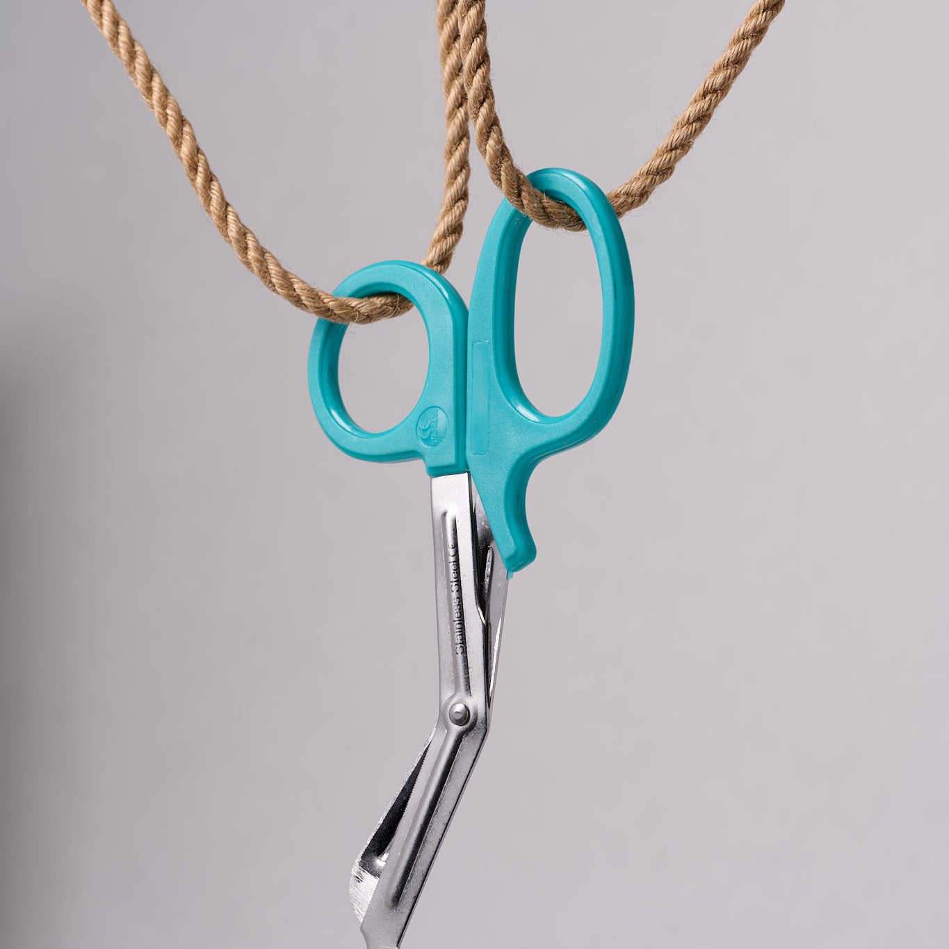 Silver emergency shears with light teal handles hanging from natural jute rope.