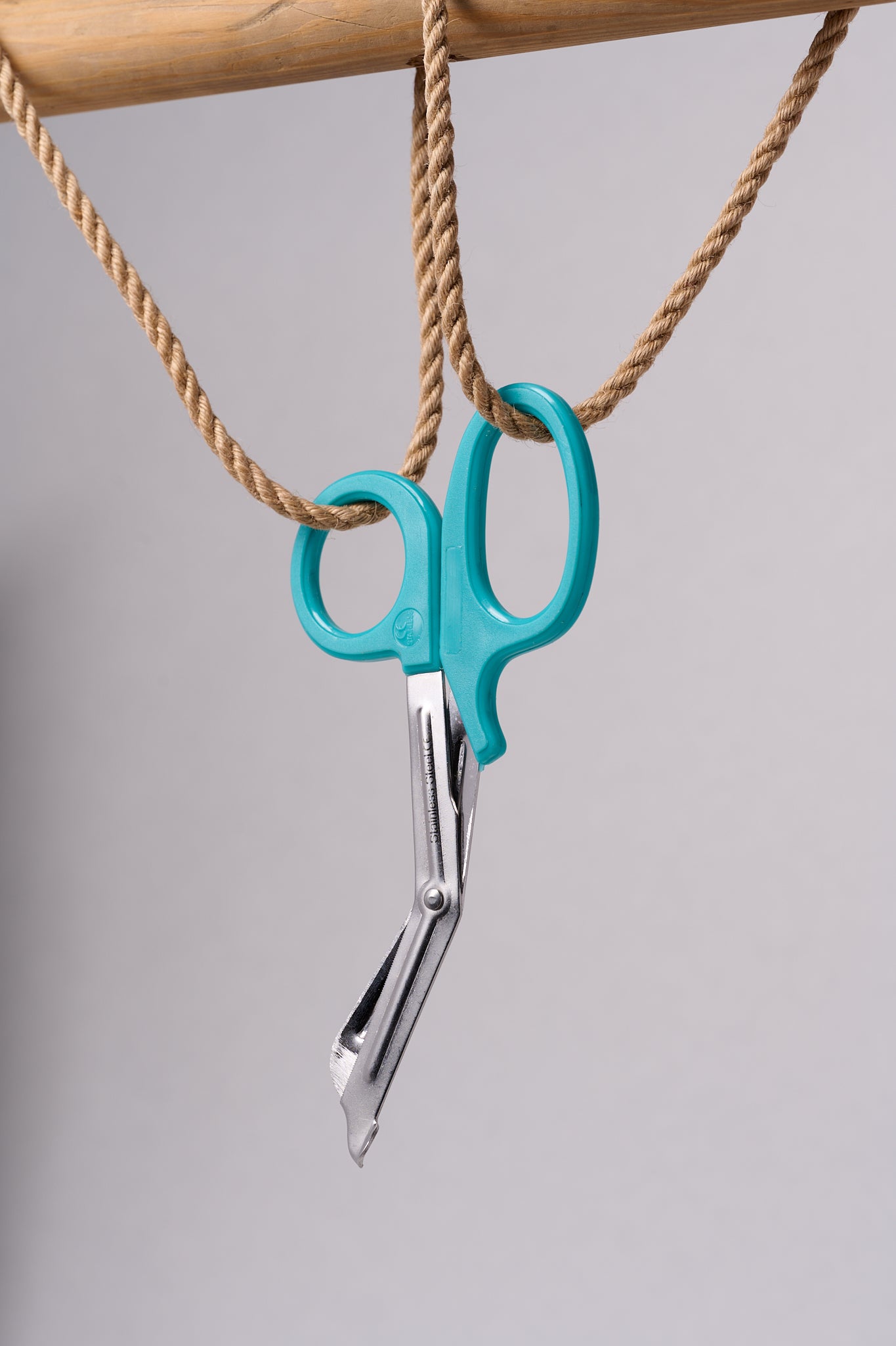 Silver emergency shears with light teal handles hanging from natural jute rope.