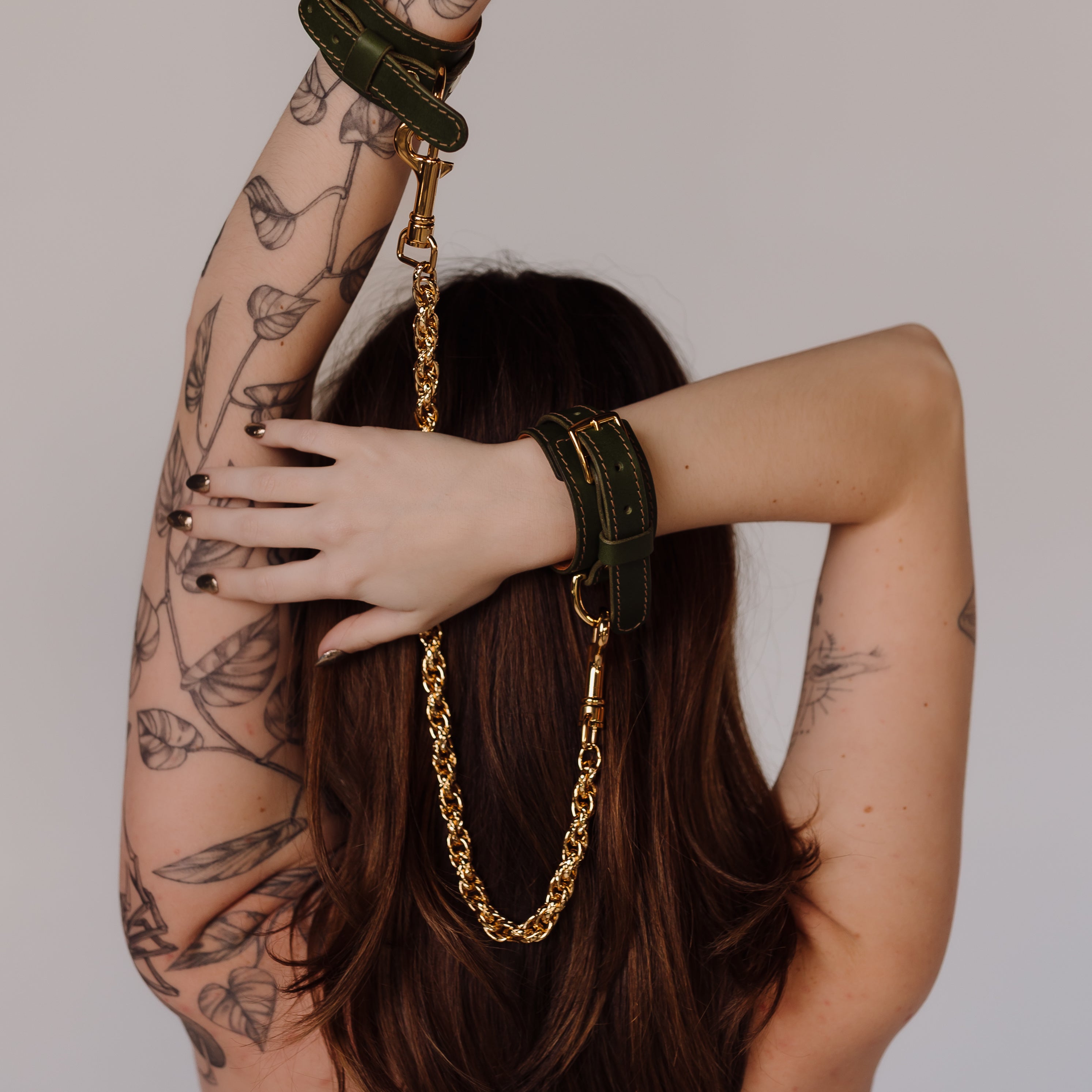 Person with tattoos wearing green bracelets with gold chain on white background