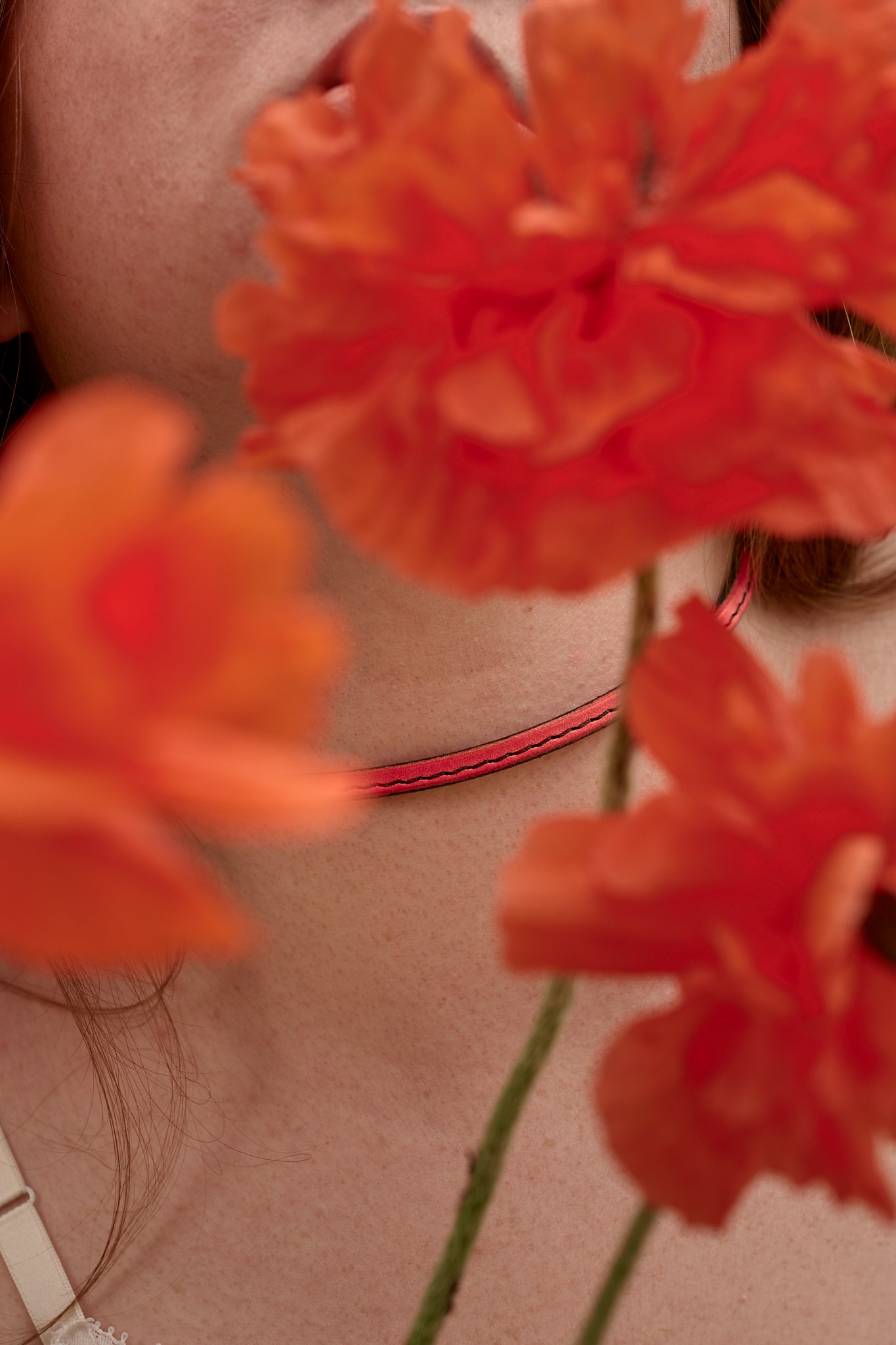 Pink leather choker necklace with orange poppies in the foreground.