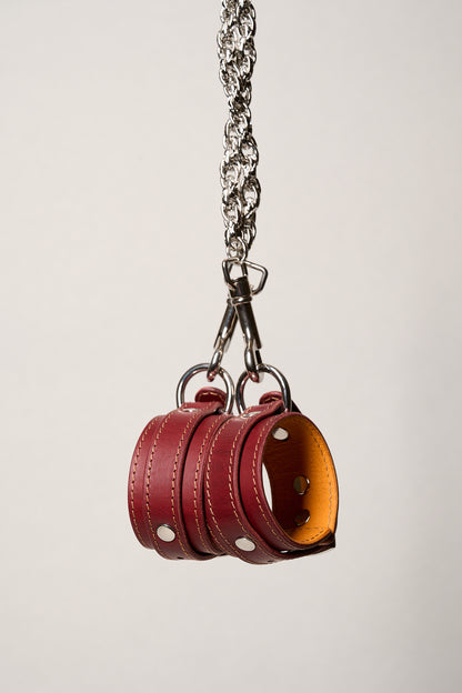 Red leather cuffs with a chain on a light gray background