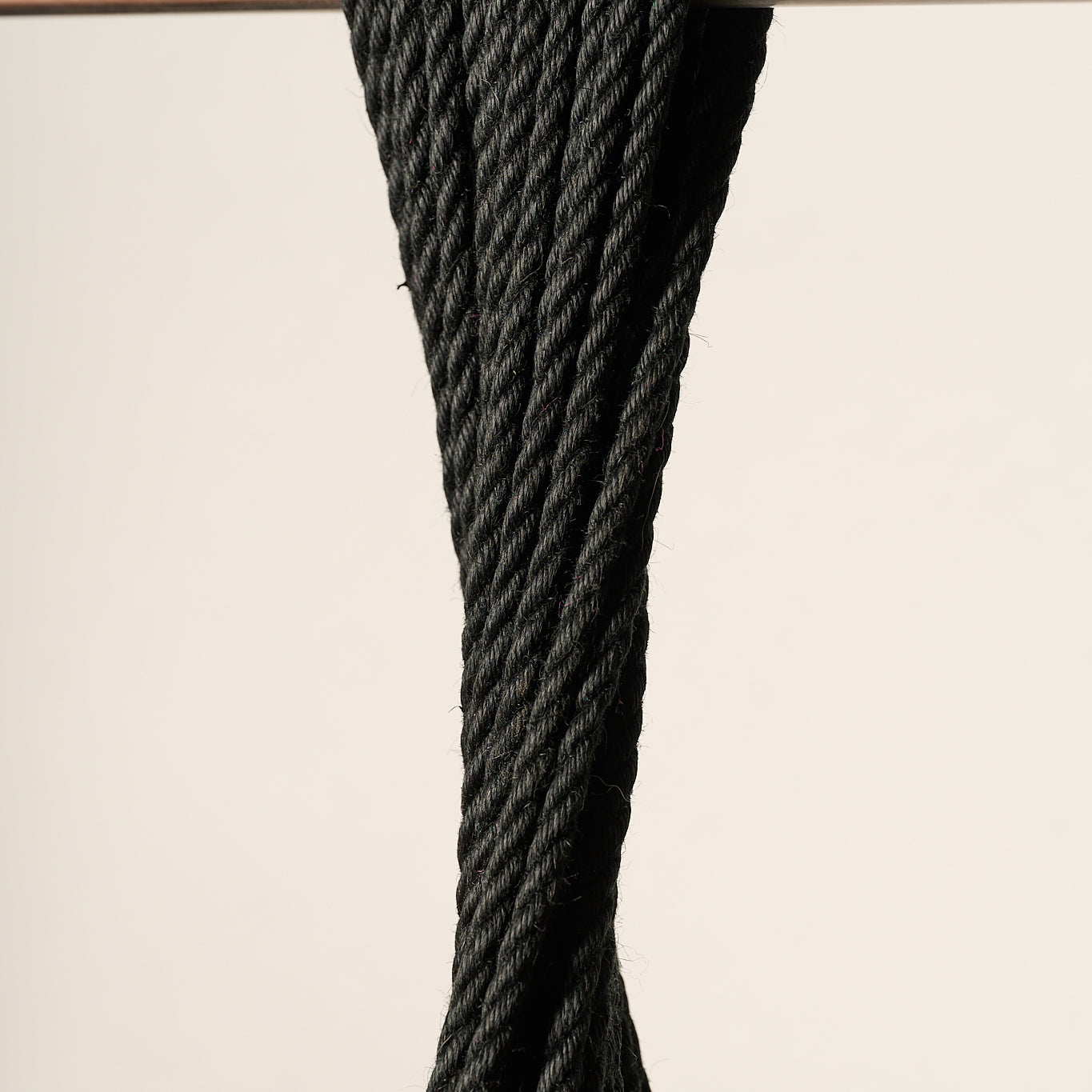 A close-up of a 6mm, jute, black twisted rope draped over a horizontal silver metal bar against a plain light beige background.
