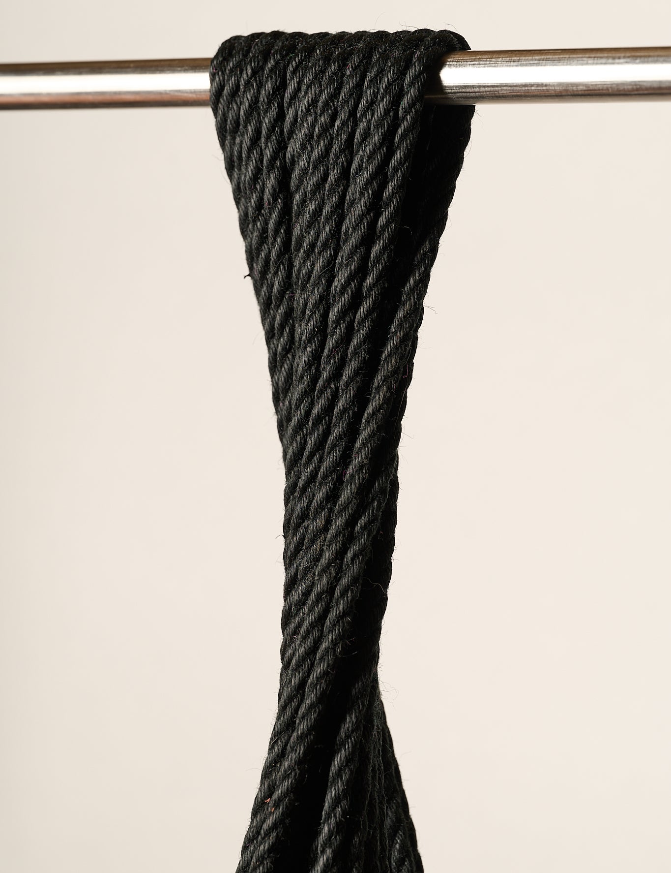 A close-up of a 6mm, jute, black twisted rope draped over a horizontal silver metal bar against a plain light beige background.