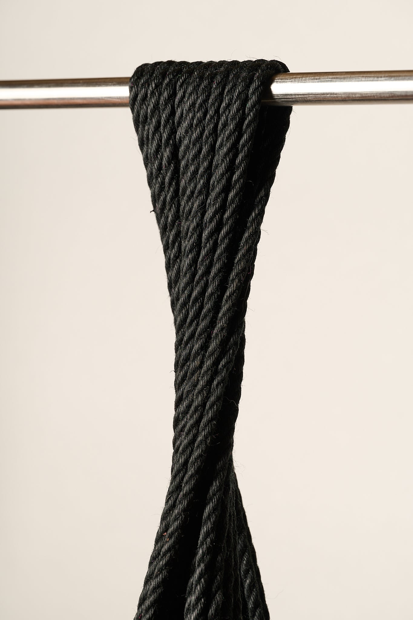 A close-up of a 6mm, jute, black twisted rope draped over a horizontal silver metal bar against a plain light beige background.