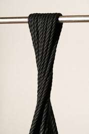 A close-up of a 6mm, jute, black twisted rope draped over a horizontal silver metal bar against a plain light beige background.
