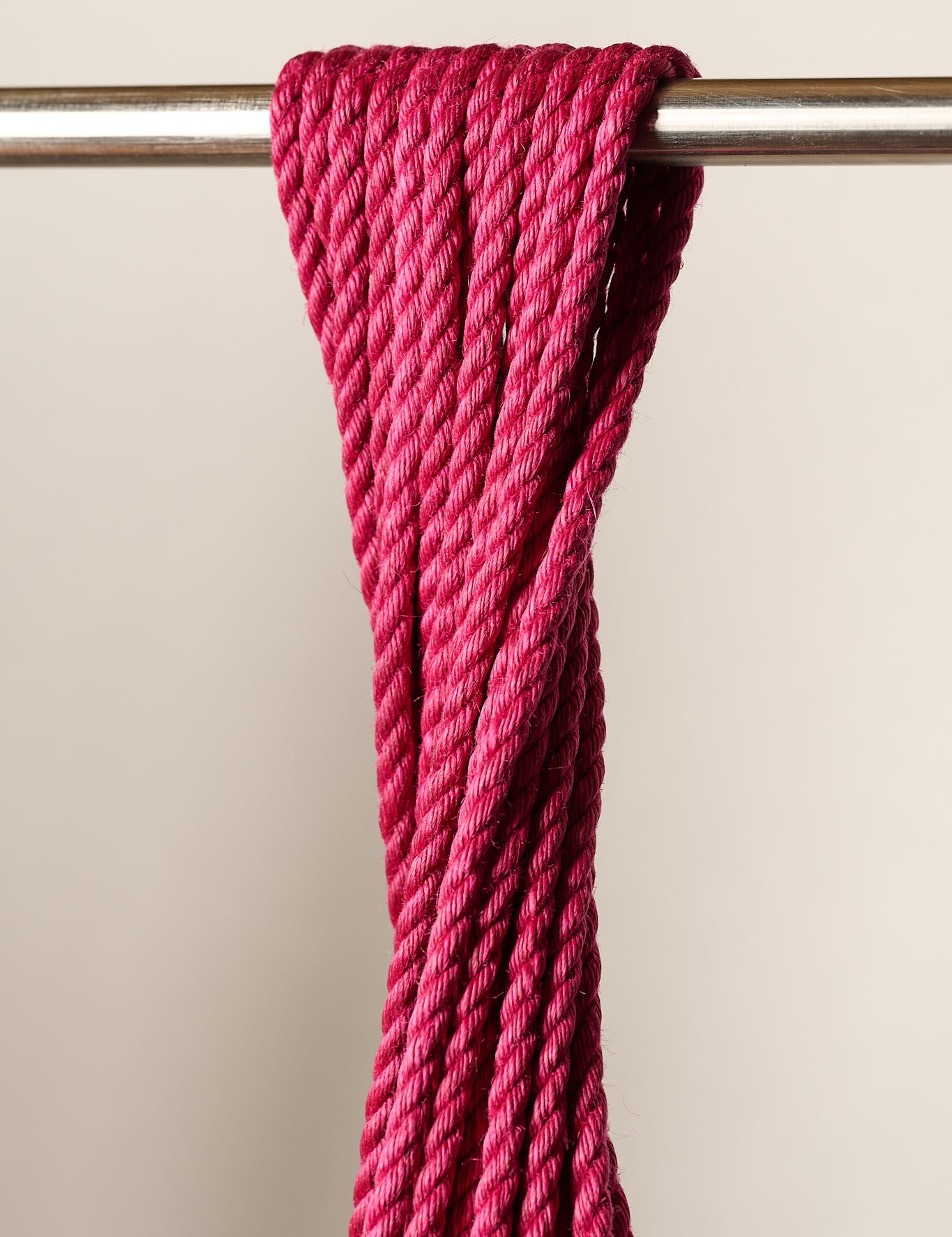 A close-up of a thick, 6mm, jute, twisted magenta pink rope draped over a horizontal metal rod against a plain light beige background.